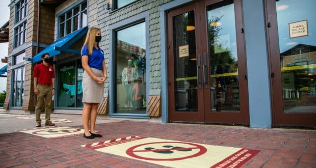 Guests wearing masks snap photos on social distancing markers outside a shuttered Disney Springs shop during the phased reopening.