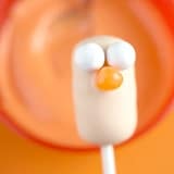 Beaker Cake Pop from The Muppets with white candy eyes and an orange beak pops against a bold orange backdrop.