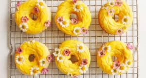 Six Rapunzel-inspired yellow donuts with pink and white flowers cool on a rack—perfect for a Disney park princess party treat.