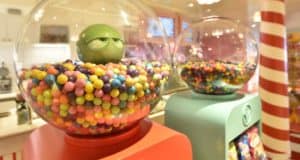 Giant gumball machines packed with bright candy; one sports a grumpy green face, adding whimsy to your Disney Cruise Line trip.