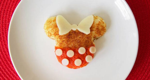 Grilled cheese toast styled like Minnie Mouse with red jam, cheese dots, and bow, served on a plate—perfect for Disney parks fans.