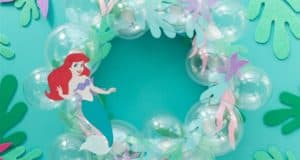 Ariel from The Little Mermaid highlights a whimsical bubble wreath with paper seaweed, perfect for Disney fans, on a teal backdrop.