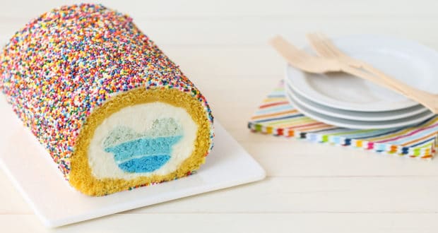 A sprinkle-covered cake roll with a Hidden Mickey-style blue and white heart inside, perfect for Disney fans, sits by party plates.