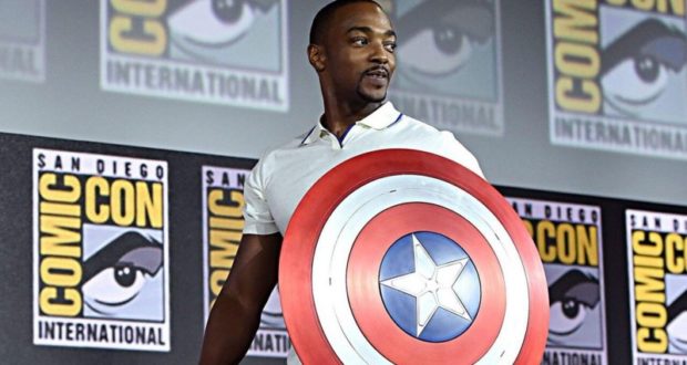 Falcon rocks Captain America's shield at San Diego Comic-Con, posing heroically before iconic Comic-Con International signage.