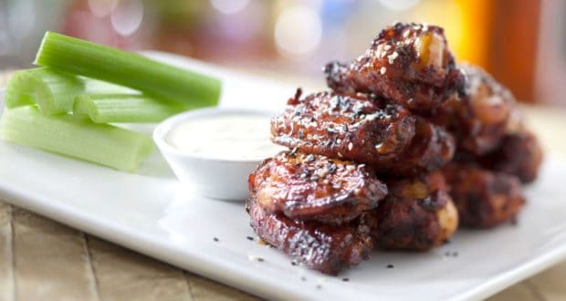 Ohana-style barbecue wings with sesame seeds, celery, and dip, just like at Disney’s Polynesian Village Resort, on a white plate.