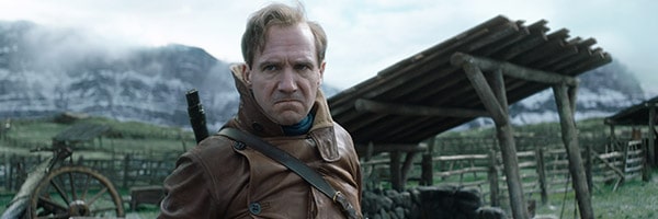 A character styled like The King’s Man stands by rustic village facades and mountain backdrops, evoking a cinematic adventure.