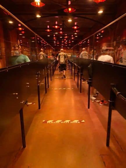 Guests line up in Disney World’s moody, red-lit queue, spaced apart for safety with visible social distancing floor markers.