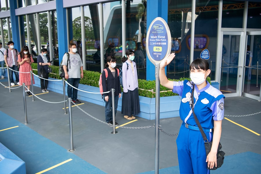 Cast Member greets guests by the wait time sign as masked visitors queue in June 2022, awaiting a refurbished Disney attraction.