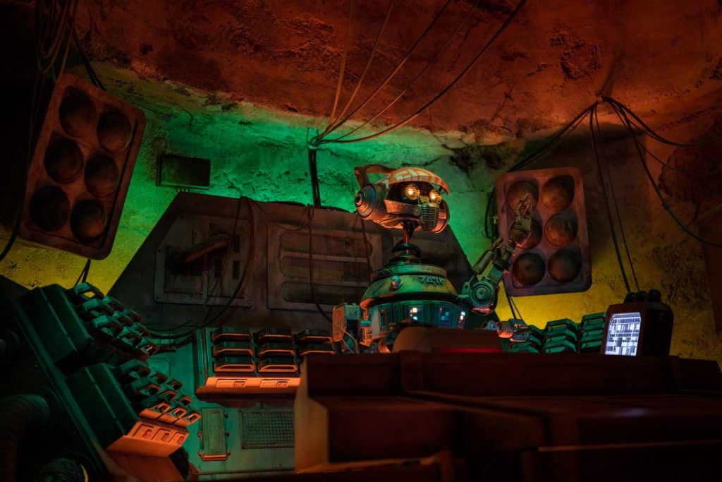 DJ R-3X spins tunes in Oga’s Cantina’s neon-lit control booth, surrounded by colorful panels—Star Wars: Galaxy’s Edge magic!.