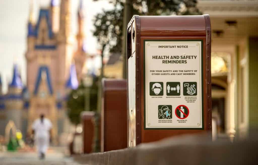 Trash can with Disney World health and safety sign, guest’s park bag visible, Cinderella Castle softly blurred in the distance.