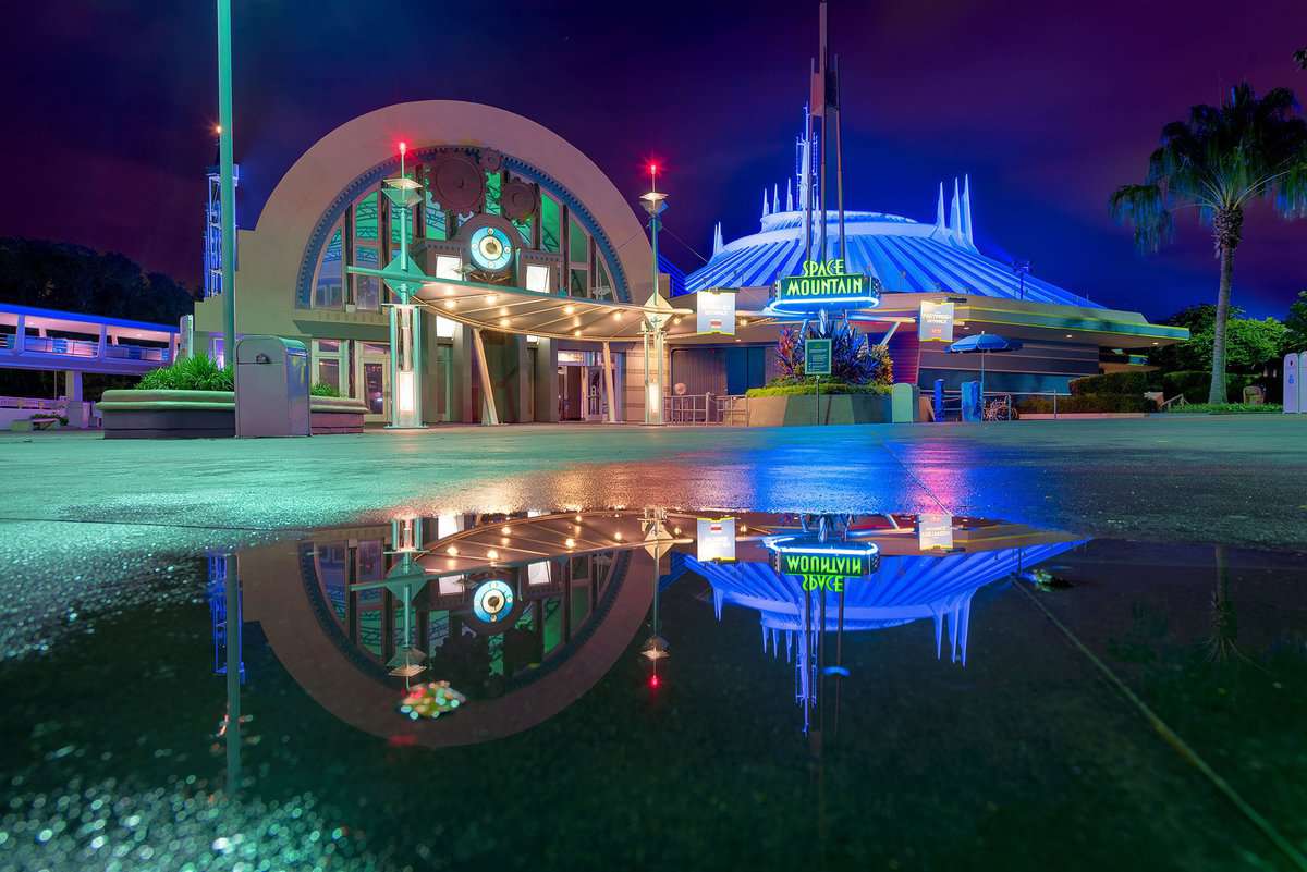 Space Mountain glows in neon at night, its reflection shimmering in a puddle—a Magic Kingdom highlight for Disney fans.