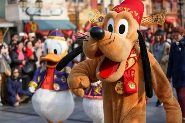 Pluto leads Donald Duck in vibrant costumes down Main Street, delighting Disney park guests during International Dog Day festivities.