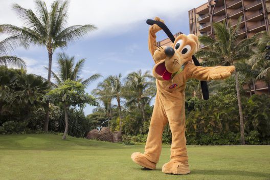 Pluto strikes a playful pose on lush grass among palm trees, bringing Disney magic to International Dog Day celebrations.