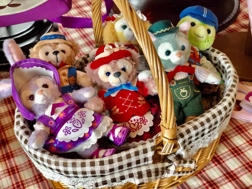 A basket of vibrant Duffy and Friends plush toys in themed outfits on a checkered tablecloth celebrates Duffy Month at Shanghai Disney Resort.