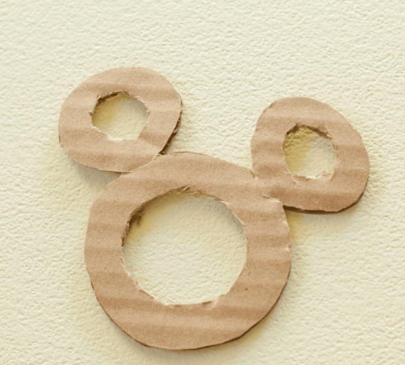 Cardboard cutout featuring three circles cleverly arranged to evoke Mickey Mouse’s iconic silhouette, displayed on a subtly textured surface—an ideal DIY craft for Disney fans looking to add a magical touch to gift wrapping with Mickey Yarn Toppers.