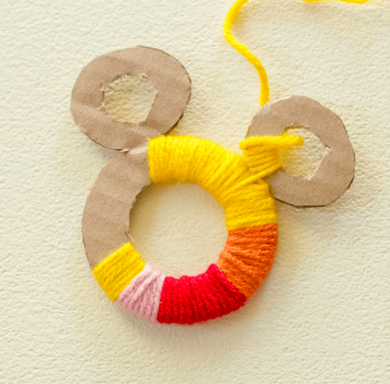 Mickey Mouse-shaped cardboard circles, partially wrapped in vibrant yarn with playful yellow tails, bring a burst of Disney magic to gifts—these handmade yarn toppers channel the whimsical spirit of Mickey at your favorite Disney parks.
