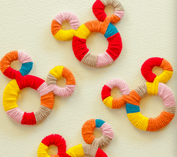 Colorful, abstract Mickey Mouse shapes crafted from yarn in red, pink, yellow, blue, and orange rest against a cream backdrop—fun souvenirs or magical DIY accents inspired by the cheerful spirit of Disney parks.