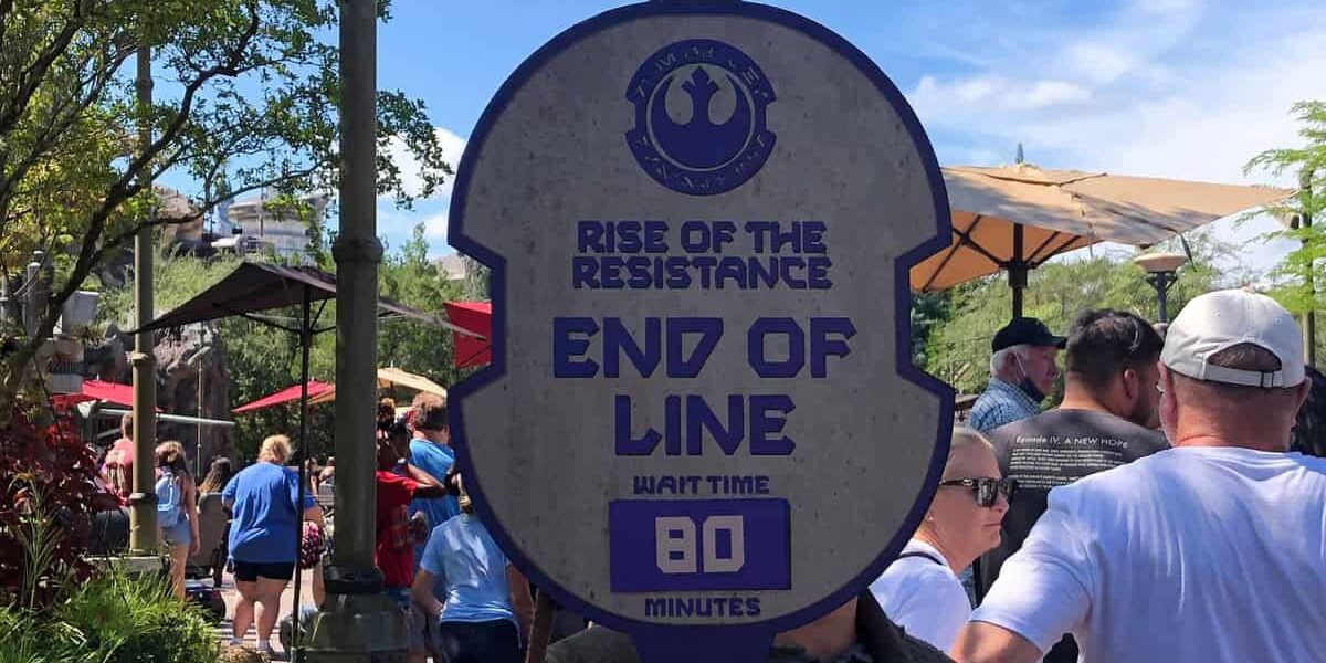 A theme park employee holds a sign reading “Rise of the Resistance End of Line, Wait Time 80 Minutes” in front of a line of people outdoors on a sunny day.