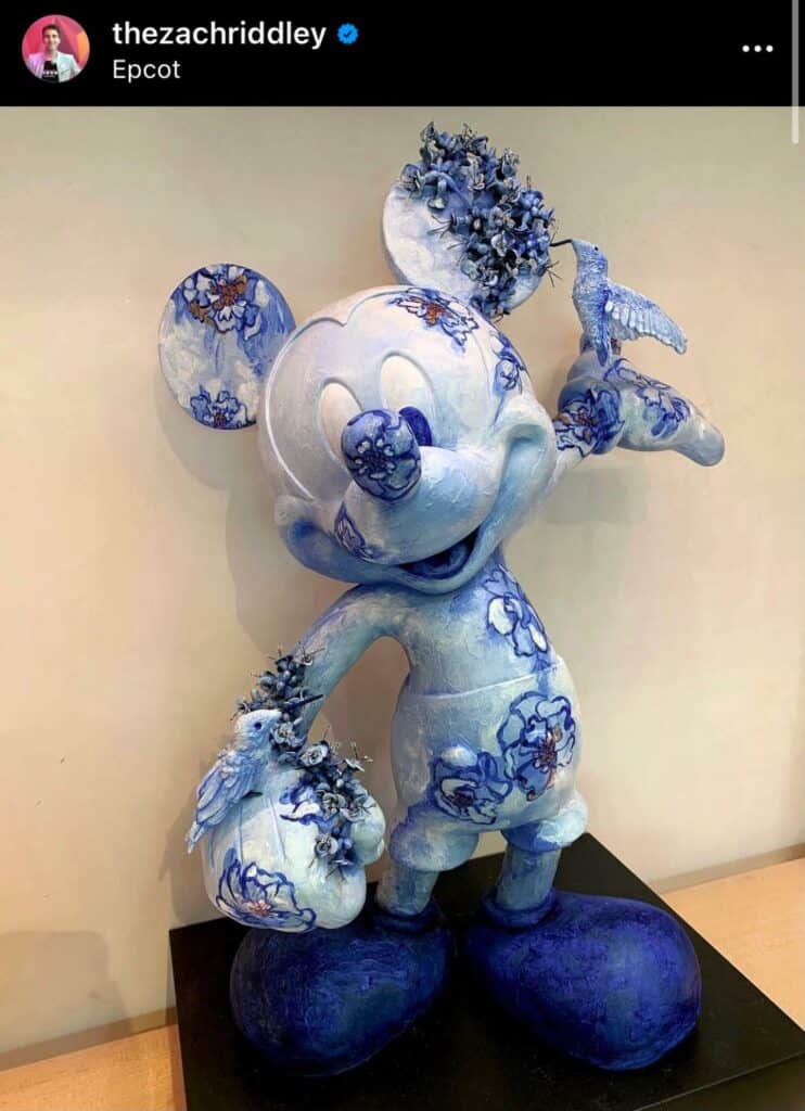Mickey Mouse takes center stage in this whimsical blue and white floral statue from the Mouse as Muse collection, holding a bird and bouquet with cheerful flowers adorning his head and hand—a charming art piece capturing Disney’s creative magic, perfect for theme park fans and collectors alike.