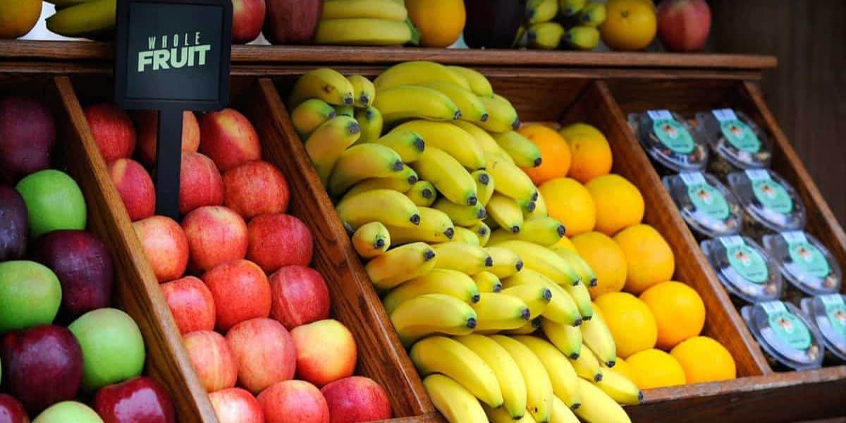 A fruit stand showcasing neatly arranged apples, bananas, oranges, and packaged produce brings a touch of healthy eating to your day. The red and green apples pop next to the ripe bananas and bright oranges. Among them, a sign reads "Whole Fruit," echoing the wholesome dining vibes of Walt Disney World.