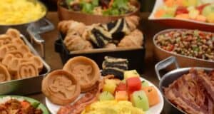 A delightful breakfast spread at Tusker House featuring Mickey Mouse-shaped waffles, scrambled eggs, bacon, sliced croissants, layered pastries, fruit salad, and a dish with mixed beans and vegetables—a magical Disney World dining experience.