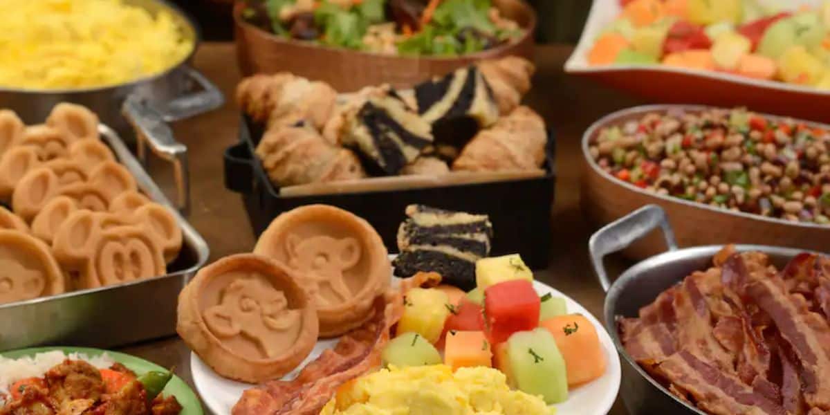 A delightful breakfast spread at Tusker House featuring Mickey Mouse-shaped waffles, scrambled eggs, bacon, sliced croissants, layered pastries, fruit salad, and a dish with mixed beans and vegetables—a magical Disney World dining experience.