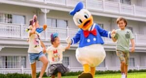 Three smiling children hold hands with Donald Duck
