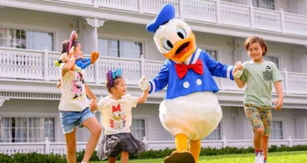Three smiling children hold hands with Donald Duck