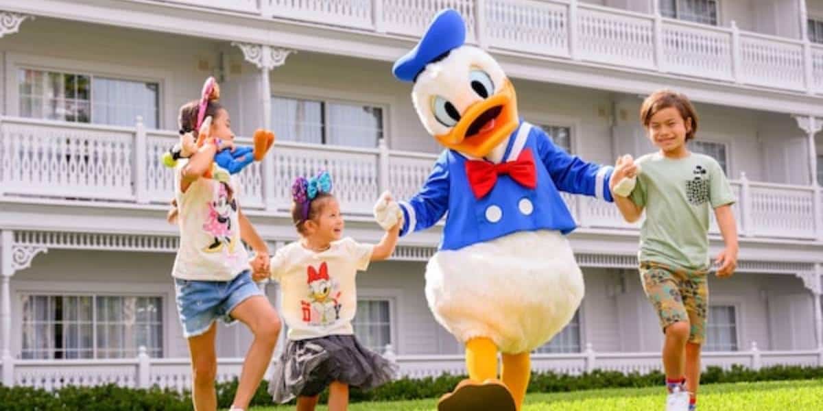 Three smiling children hold hands with Donald Duck