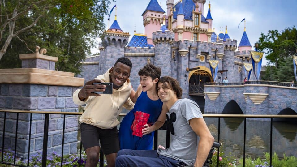 three guests taking a selfie outside the castle, one is in a wheelchair