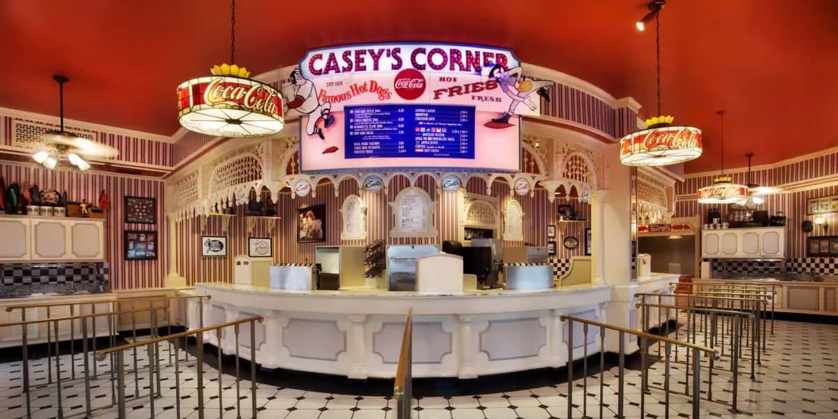 Casey's Corner, one of My Favorite Eats Money Can Buy at Walt Disney World, is a nostalgic diner with a vintage baseball theme. The interior features a large menu board, Coca-Cola signs, white counters, and tiled floors. Classic diner elements like barstools, retro lighting, and memorabilia complete the charm.