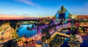 A vibrant, colorful sunset view of the Walt Disney World Swan Dolphin Food & Wine Classic resort with a pyramid-shaped building, palm trees, water features, and illuminated walkways, creating a lively tropical atmosphere.