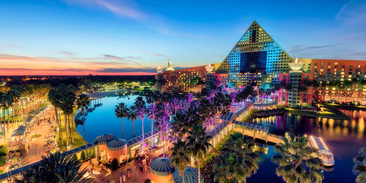 A vibrant, colorful sunset view of the Walt Disney World Swan Dolphin Food & Wine Classic resort with a pyramid-shaped building, palm trees, water features, and illuminated walkways, creating a lively tropical atmosphere.