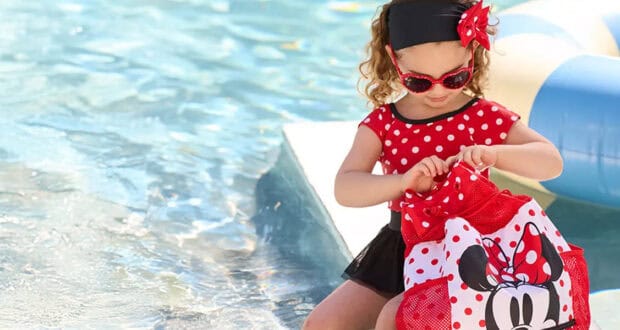 A young girl in a red polka-dot dress, headband, and sunglasses sits by a pool, opening a Minnie Mouse bag—perfect for any Disney vacation packing list. An inflatable pool float is visible in the background.