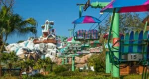 Experience a colorful chairlift ride over a lush, tropical amusement park landscape, with snowy Blizzard Beach-themed structures in the background. Bright skies and vibrant greenery evoke the festive spirit of Christmas in this playful scene.