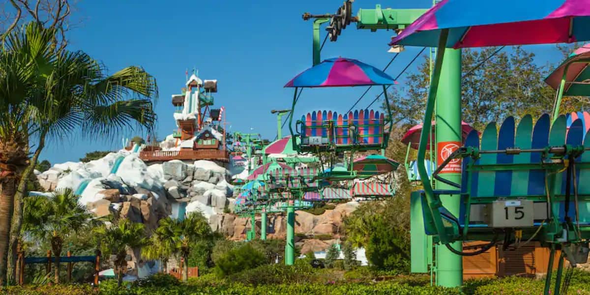 Experience a colorful chairlift ride over a lush, tropical amusement park landscape, with snowy Blizzard Beach-themed structures in the background. Bright skies and vibrant greenery evoke the festive spirit of Christmas in this playful scene.
