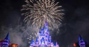 Fireworks explode in the night sky above a brightly lit castle with blue and purple lights at Disney World. The disney world fireworks create a festive and magical scene, with illuminated turrets and sparkling effects.