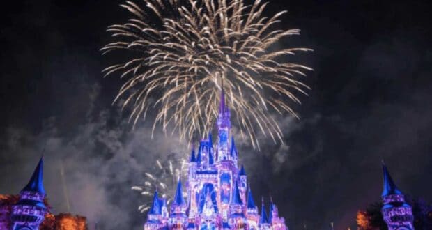Fireworks explode in the night sky above a brightly lit castle with blue and purple lights at Disney World. The disney world fireworks create a festive and magical scene, with illuminated turrets and sparkling effects.