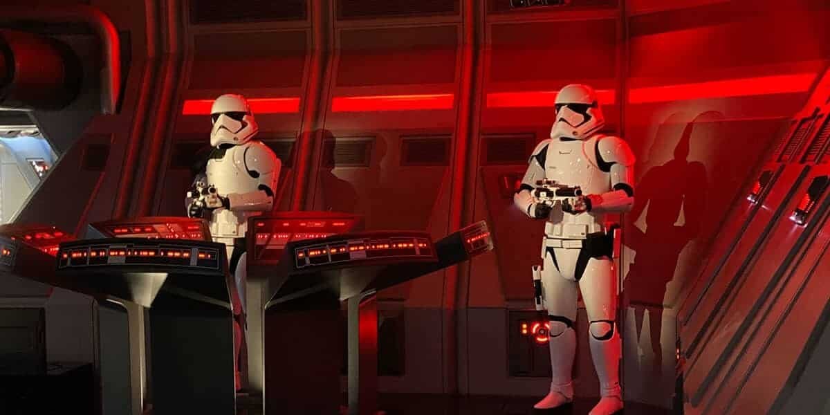 Two Stormtroopers in white armor stand guard inside a spaceship control room with red lighting, standing beside futuristic control panels glowing with red lights.