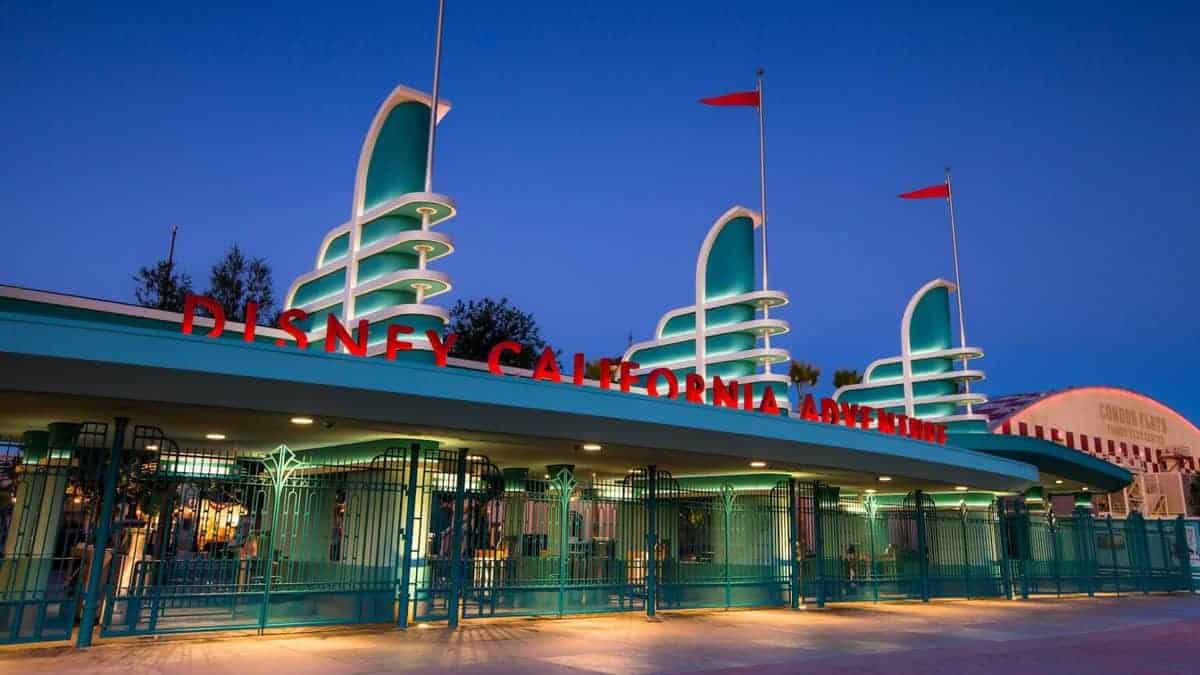 Disney California Adventure entrance at sunset, featuring iconic teal art deco gates and brightly illuminated marquee welcoming guests into the park.