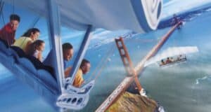 A group of people on the Soarin' ride at EPCOT simulates flying over the Golden Gate Bridge, with passengers smiling and leaning forward. The scene includes a blue sky and ocean below, capturing all the exhilaration of this aerial adventure.