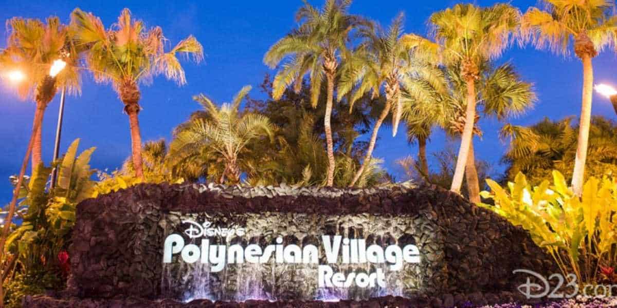 Illuminated sign of disney's polynesian village resort at night surrounded by lush palm trees and tropical plants.