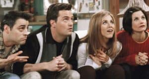 Four people sit closely together on a couch, attentively looking upwards. They appear to be engaged or surprised. The person on the far left wears a plaid shirt, the next in a jacket, followed by someone in a white top, and the last in a red sweater—possibly reacting to news of the Matthew Perry death investigation.