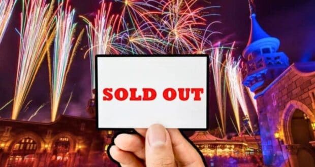 A hand holds a white sign with "SOLD OUT" written in red letters against a vibrant background of colorful fireworks illuminating the night sky above a Disney fantasy castle.