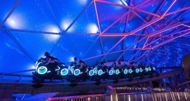 A futuristic roller coaster ride at Disney World features neon-lit vehicles resembling motorcycles under a large, glowing blue and purple canopy. Riders speed along the track, creating an exciting and dynamic atmosphere that captures the magic of adventure.