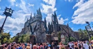 A bustling crowd of visitors under a clear sky at a theme park featuring a large, impressive castle modeled after hogwarts from the harry potter series.