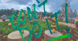 A vibrant amusement park scene is overlaid with bright green graffiti text reading "DON'T DO IT!". The background features cheerful gold sculptures, crowds of people on their trips, and a fanciful castle under a partly cloudy sky reminiscent of Disney World.