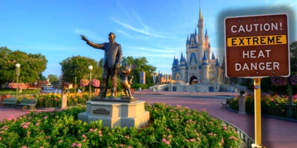 A statue of a man and a mouse stands in a garden near a castle, with clear blue skies overhead. A sign nearby reads "CAUTION! EXTREME HEAT DANGER," indicating potential weather hazards in the area. The scene has that magical Disney theme park charm.