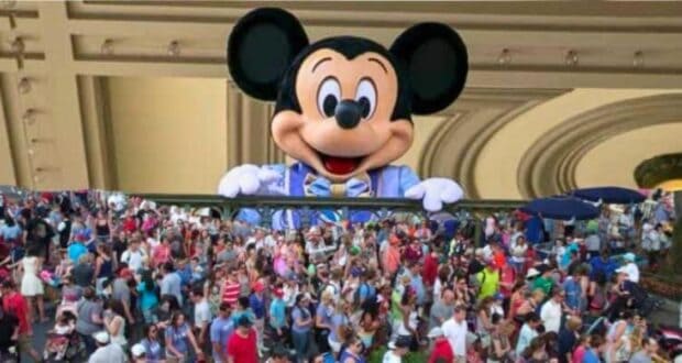 Mickey Mouse, a Disney character, peeking over a ledge above a dense crowd of visitors at a theme park.