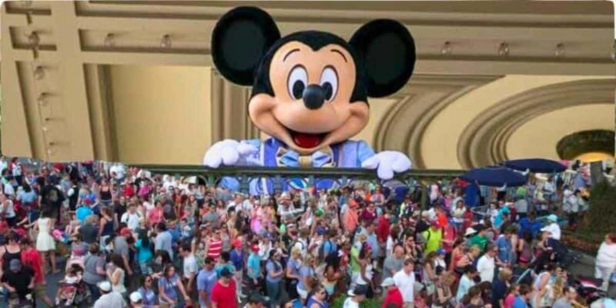 Mickey Mouse, a Disney character, peeking over a ledge above a dense crowd of visitors at a theme park.